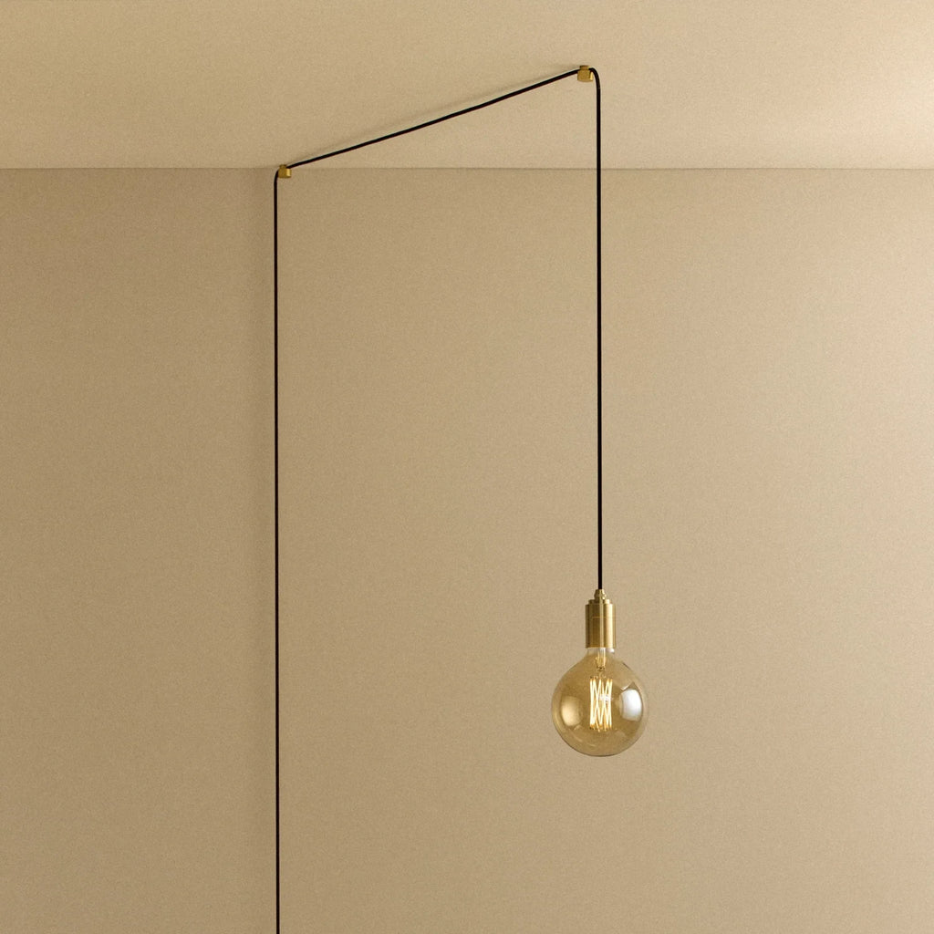 Tinted filament globe plug-in pendant, in brass, routed across the ceiling and down the wall
