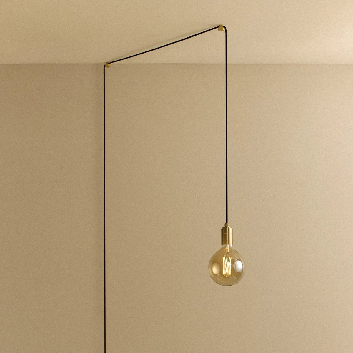 Tinted filament globe plug-in pendant, in brass, routed across the ceiling and down the wall