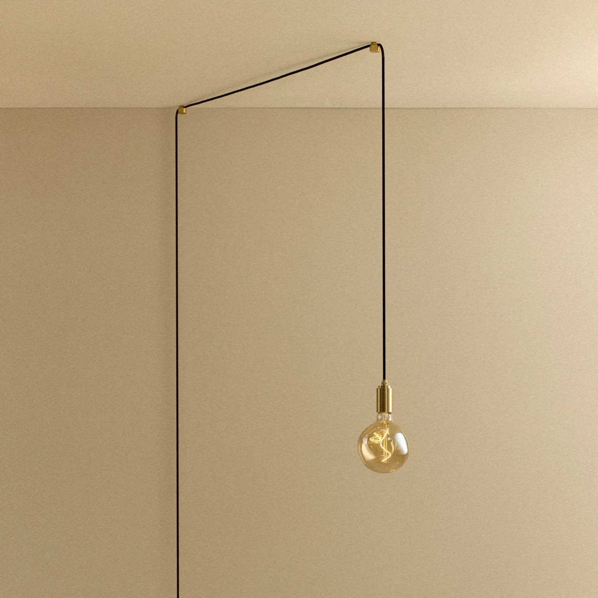 Tinted globe bulb plug-in pendant, in brass, routed across the ceiling and down the wall