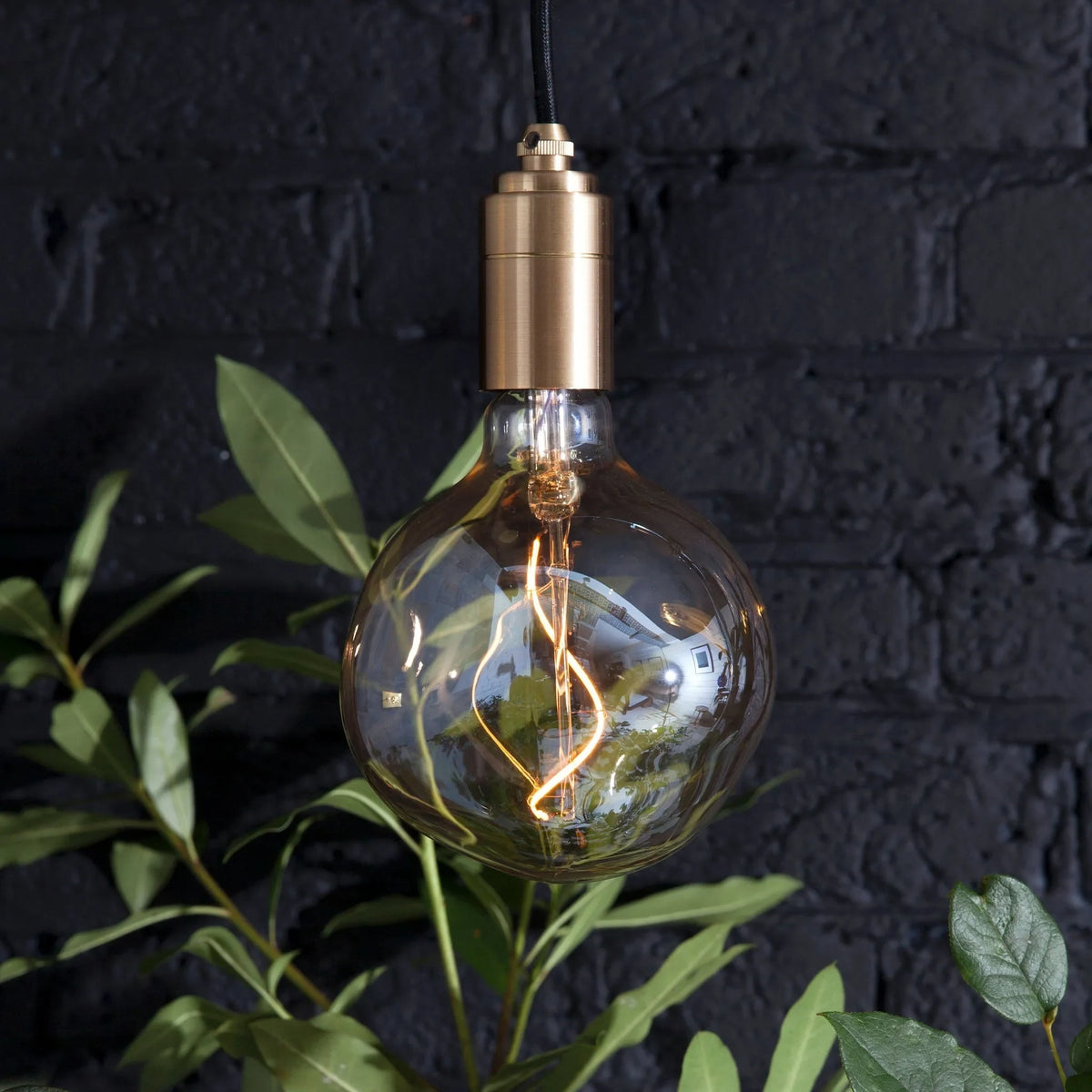 Tinted globe bulb plug-in pendant, lit against a dark brick wall