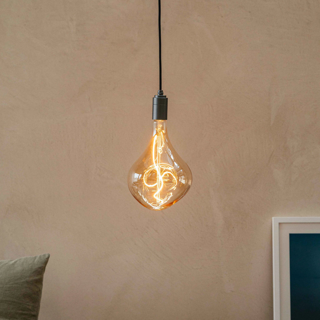 Plug-in pendant with tinted organic bulb, graphite, close-up of the lit bulb against a plain wall