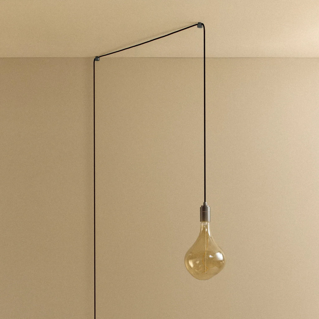 Plug-in pendant with tinted organic bulb, graphite, lit, hung from a wall node, another angle