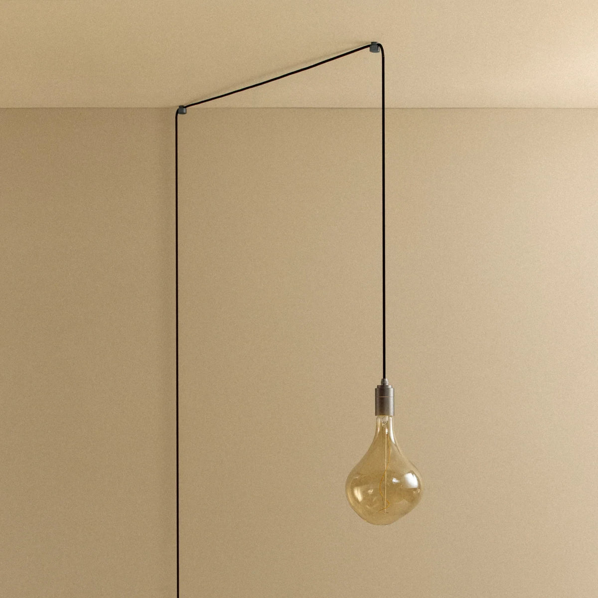 Plug-in pendant with tinted organic bulb, graphite, lit, hung from a wall node, another angle