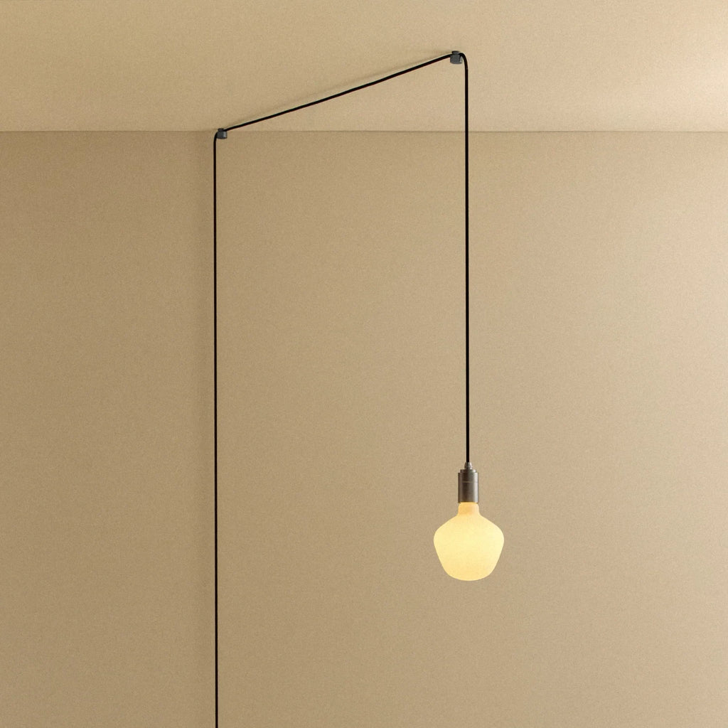 Plug-in pendant with a trapezoid matte white glass bulb, graphite, lit, hung from a ceiling corner