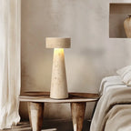 Natural travertine mushroom table lamp lit on a wooden stool beside a bed
