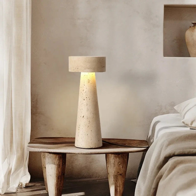 Natural travertine mushroom table lamp lit on a wooden stool beside a bed