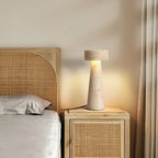 Travertine table lamp on a rattan bedside cabinet in a calm bedroom