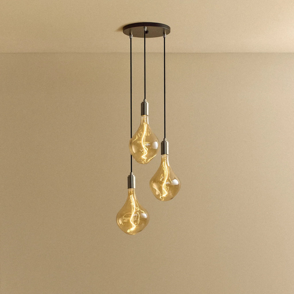 Triple cluster pendant with tinted sculptural bulbs, lit, against a plain wall
