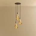 Triple cluster pendant with tinted sculptural bulbs, lit, against a plain wall