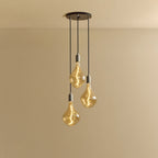 Triple cluster pendant with tinted sculptural bulbs, lit, against a plain wall