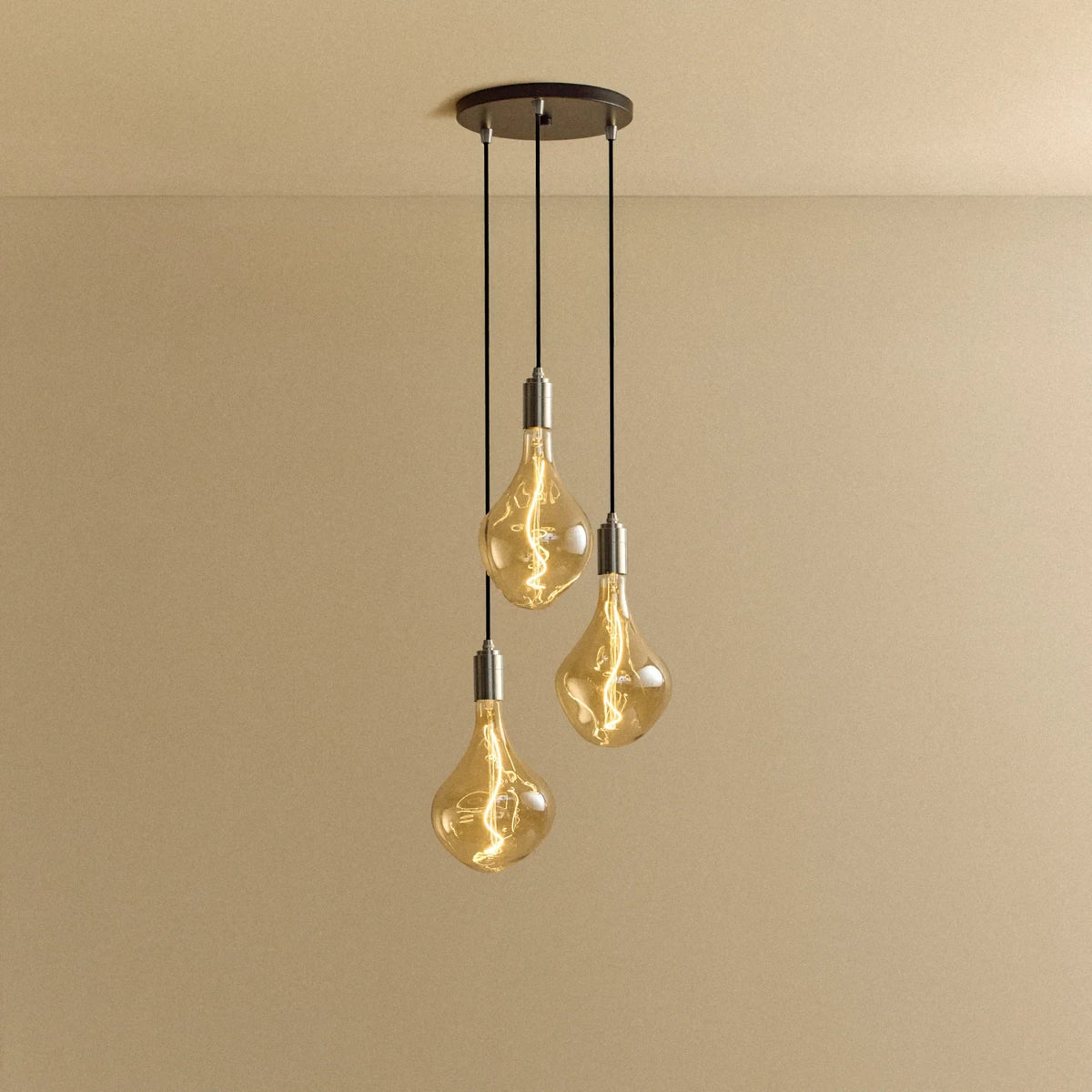 Triple cluster pendant with tinted sculptural bulbs, lit, against a plain wall