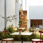 Triple cluster pendant with tinted sculptural bulbs, above a table by a garden
