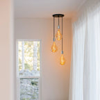 Triple cluster pendant with tinted sculptural bulbs, in the corner of a bright room
