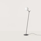 Twig branch floor lamp with opal glass globe, in matte black, on a plain background