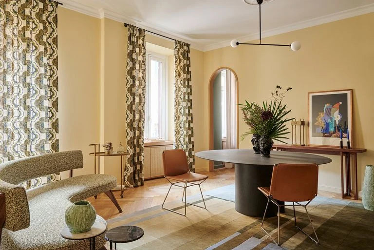 Two-globe pendant with horizontal arm, in black, above a dining table in a patterned room