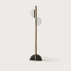 Aged gold column floor lamp with two scalloped opal shades, on a half-round black marble base, against a plain wall