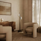 Aged gold column floor lamp with two scalloped opal shades, beside an armchair in a living room