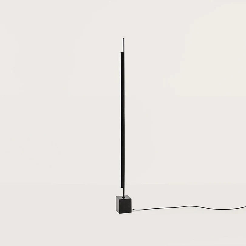 Vertical LED bar floor lamp with black marble cube base, on a black marble cube, against a plain wall