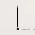 Vertical LED bar floor lamp with black marble cube base, on a black marble cube, against a plain wall
