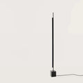 Vertical LED bar floor lamp with black marble cube base, on a black marble cube, against a plain wall, second view