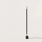 Vertical LED bar floor lamp with black marble cube base, on a black marble cube, against a plain wall, second view