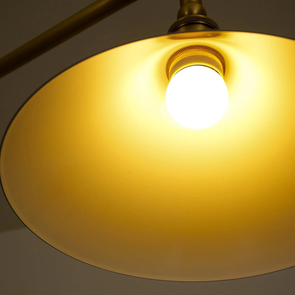 Two-light gold bar pendant with white cone shades, lit from below