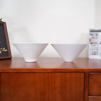 Two-light gold bar pendant with white cone shades, spare shades on a sideboard