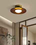 Low profile walnut and gold flush ceiling light, lit near a glass door