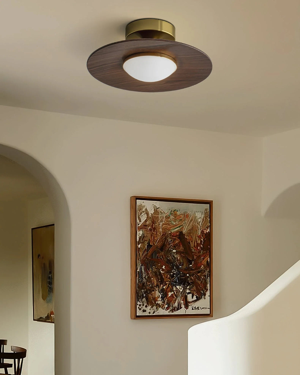 Low profile walnut and gold flush ceiling light, lit in an arched hallway