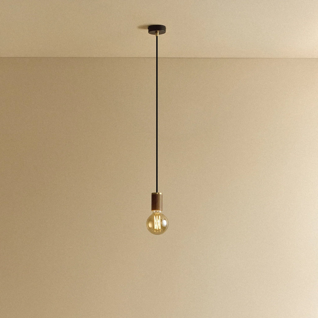 Walnut pendant with tinted glass filament bulb, lit, against a plain wall