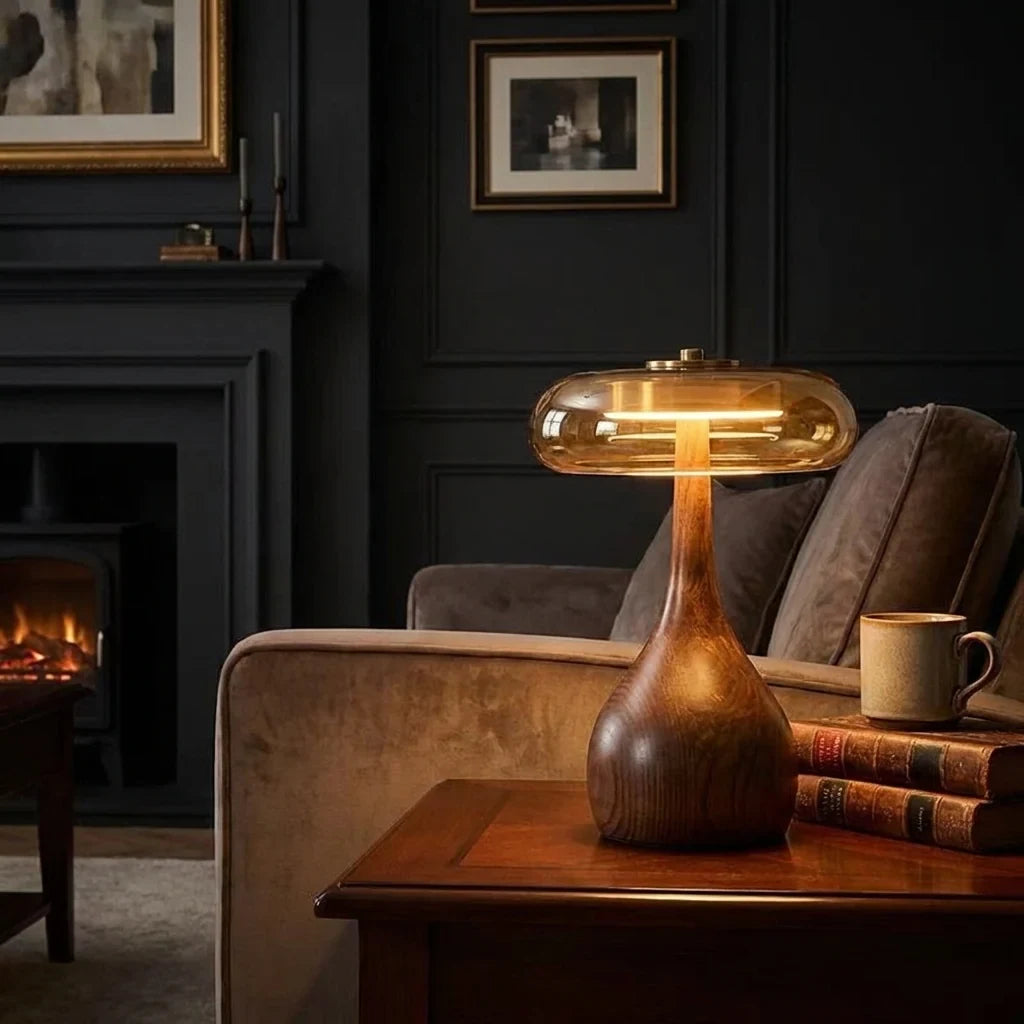 Walnut-tone timber table lamp with a tinted glass disc, lit on a side table by a fireplace