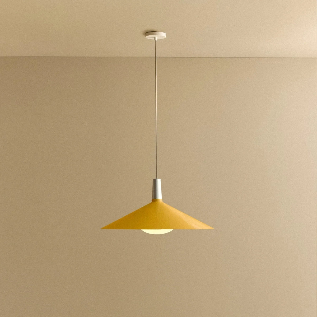 Large yellow wide steel pendant with oval bulb, against a plain wall