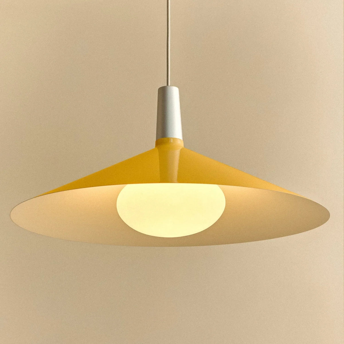 Large yellow wide steel pendant with oval bulb, close-up of the lit shade and bulb
