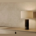 Wood and marble table lamp with drum shade, in black wood and black marble, on a shelf